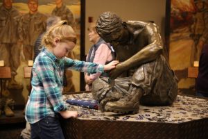 A young girl touches ‘The Silent Battle’ sculpture that reflects the struggles of returning combat veterans.